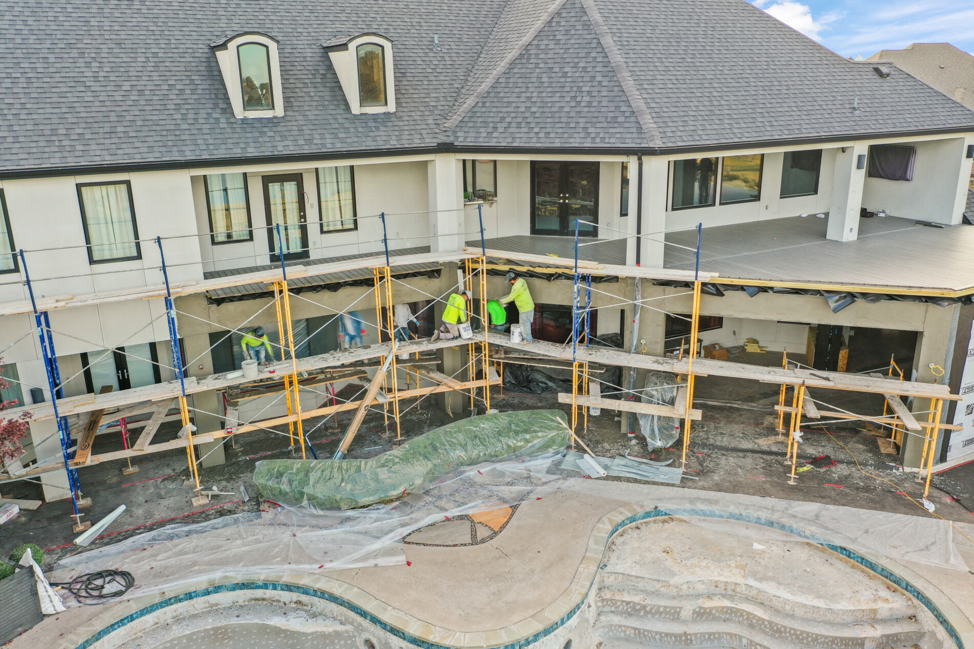 Close view of construction crews working along the back of the Shadow Valley home, with scaffolding installed and the unfinished pool in the foreground.