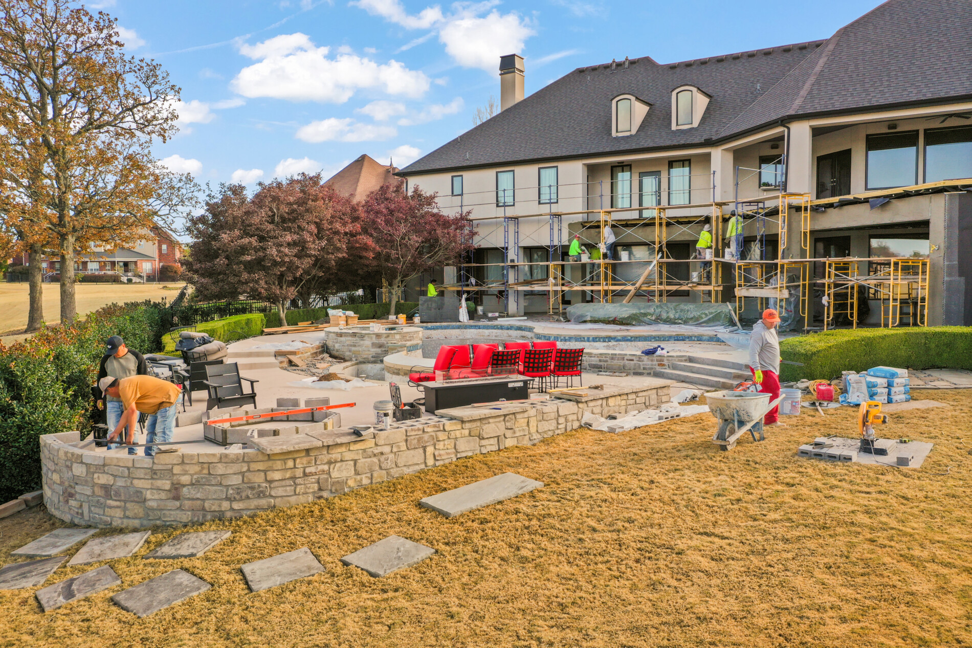 Mid-range view of the Shadow Valley backyard during a comprehensive renovation, showing the in-progress pool structure, stonework, and exterior home updates.
